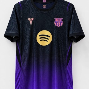 May include: A short-sleeve athletic jersey featuring a dark navy and purple gradient design with a snakeskin-like texture. The front displays a gold Spotify logo, a pink and blue FC Barcelona crest, and a pink Kobe Bryant sheath logo on the chest.