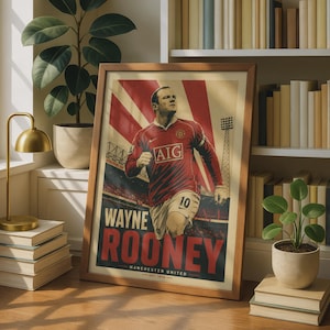 May include: A framed poster featuring a graphic illustration of Wayne Rooney in a red Manchester United jersey with the text AIG, 10, WAYNE ROONEY, MANCHESTER UNITED, and EST. 1878. The background shows a stadium with red and white rays.