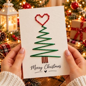 Puede incluir: Una tarjeta de felicitación blanca con un diseño de árbol de Navidad bordado a mano con hilo verde, rematado con un corazón de hilo rojo. El tronco está hecho con hilo marrón. El texto Merry Christmas está impreso en negro bajo el árbol.