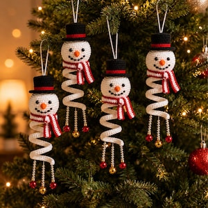 May include: Four crocheted snowman ornaments hanging from white strings. Each snowman has a black top hat with a red band, an orange nose, a black stitched smile, and a red and white striped scarf. A white spiral body ends in beaded tassels.