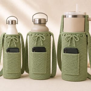 May include: Three sage green crocheted water bottle holders with adjustable drawstring closures, integrated shoulder straps, and small front pockets containing black smartphones. Each holder features a textured stitch pattern and fits a different bottle size.