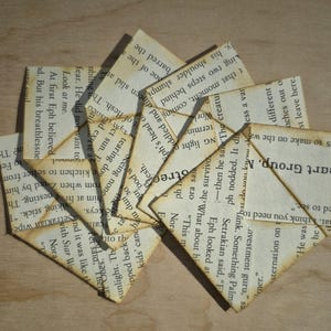 May include: A collection of triangular corner bookmarks crafted from vintage book pages with visible black printed text. The paper edges are aged with a brown tint, and the bookmarks are arranged in a layered, overlapping fan-like pattern.