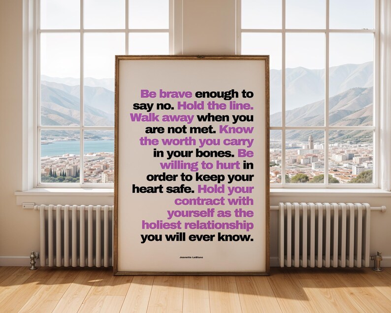 Purple and black boundary print in a thin dark wood frame standing on a pale wood floor in front of a tall window with a view of mountains, a lake, and a hillside town, between two white radiators. Bright, clear daylight fills the room. A calm, open setting for counselor office decor in a practice with big windows, where clients can sit, breathe, and talk.