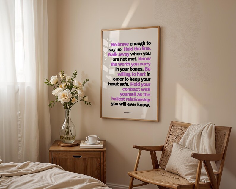 Purple and black boundary print in a light wood frame hanging above a wood nightstand with a glass vase of white roses, a white teacup, and a book, beside a woven rattan chair with a cream pillow and throw. Soft light comes through sheer curtains onto a bed with cream linen. A calm bedroom setting for a self trust print, a daily reminder written by Jeanette LeBlanc to keep your own promises.