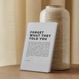 May include: A hardcover book with the title "FORGET WHAT THEY TOLD YOU" in bold black text. The book is propped up against a beige, textured vase. The book's pages contain additional text in a smaller font.
