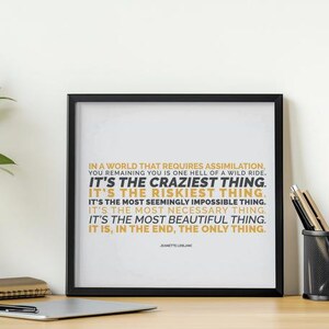 You Remaining You printable shown in a black frame leaning against a white wall on a light wood desk, beside a silver laptop, a black mesh cup of pencils, a small stack of notebooks, and a leafy plant at the edge. Clean, bright daylight. Home office styling for an uplifting quote. A motivational printable for a desk where you do your own work your own way, with the line It is, in the end, the only thing in gold capitals.