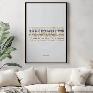 You Remaining You printable shown in portrait layout in a black frame hanging on a soft gray plaster wall above a cream sofa with cream pillows, beside a large banana leaf plant, dried pampas grass, and a small woven basket. The gold and black text sits near the top of the page. Calm living room styling. An independent woman reminder for over the sofa, and a digital download wall art piece you can print to fit your own frame.