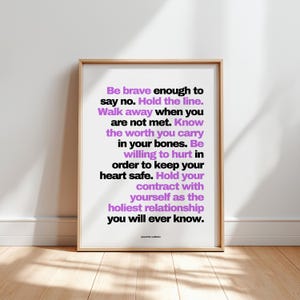 Purple and black boundary print in a light wood frame leaning against a plain white wall on a pale wood floor, with soft window light and leaf shadows across the floor. Every line is easy to read here, from Be brave enough to say no down to you will ever know, signed Jeanette LeBlanc. A bold typography print for a minimalist room, printable at home or at a print shop in the size you need.