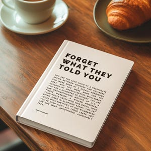 May include: A hardcover book titled "FORGET WHAT THEY TOLD YOU" with text on the cover and inside. A cup of coffee and a croissant are on a wooden table. The book is white with black text.