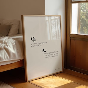 May include: A framed print with a light wood frame. The print has a white background with black text that reads "Q. what's your guilty pleasure?/ A. i no longer believe in feeling guilty about pleasure/."