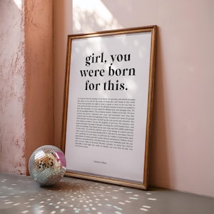 May include: A framed print with the text "girl, you were born for this." in a gold frame. A disco ball sits on the floor in front of the print. The print is on a wall with a pinkish-beige texture.