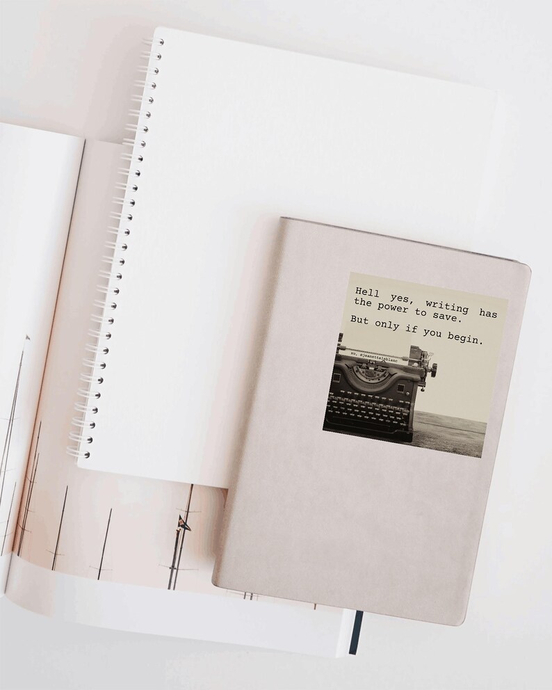 Beige notebook decorated with a sticker reading “Hell yes, writing has the power to save. But only if you begin.” Featuring a vintage typewriter, this Jeanette LeBlanc quote inspires creative courage and writing encouragement.