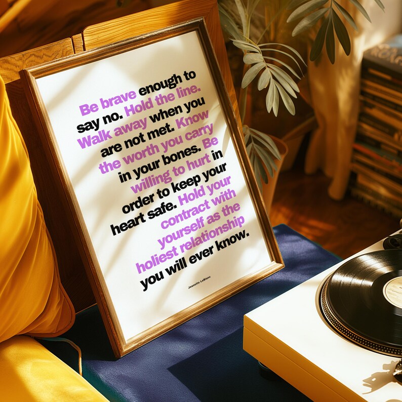 Purple and black boundary print in a light wood frame propped at an angle beside a mustard yellow cushion and a white record player with a black vinyl record on a navy surface, with a leafy plant and a record shelf behind. Warm sun and leaf shadows cross the bold text. A retro wall art look for a music corner, and a breakup gift for her when she needs the line Be willing to hurt in order to keep your heart safe.