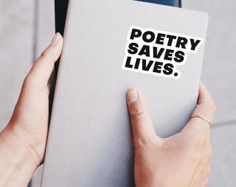 Può includere: Un taccuino grigio chiaro con un adesivo bianco e nero che recita "POETRY SAVES LIVES". Un taccuino blu scuro è dietro il taccuino grigio. I taccuini sono tenuti da una persona.