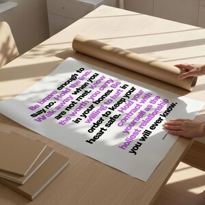 Two hands unroll a large printed copy of this boundary poster on a pale wood desk next to a roll of brown kraft paper and a stack of tan notebooks, in bright window light. The bold black and purple sans serif text runs sideways across white paper. Shows the digital file printed at poster size. A boundaries print to hang where you practice saying no, at home, in a therapist office, or at work.