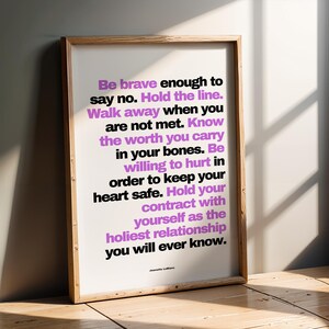 Purple and black boundary print in a weathered natural wood frame leaning against a gray wall on a wood floor, with strong window light and shadows crossing the frame. The contrast makes the bold purple words Hold the line stand out. A strong statement print for a hallway or entry, and an encouragement print for a friend who is working on saying no without explaining herself.