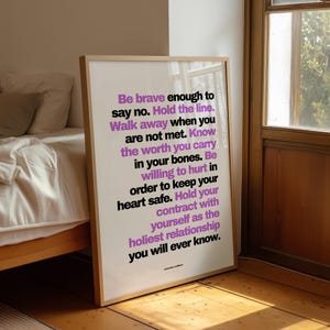 May include: A framed print with a light wood frame, leaning against a wall. The print features inspirational text in black and purple, including the phrases "Be brave enough to say no" and "Hold the line."
