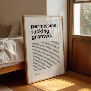 Peut inclure: Une affiche encadrée avec les mots "permission. fucking. granted." en gros caractères noirs. En dessous, un texte plus petit énumère des affirmations. L'œuvre est exposée dans une pièce avec de la lumière naturelle.