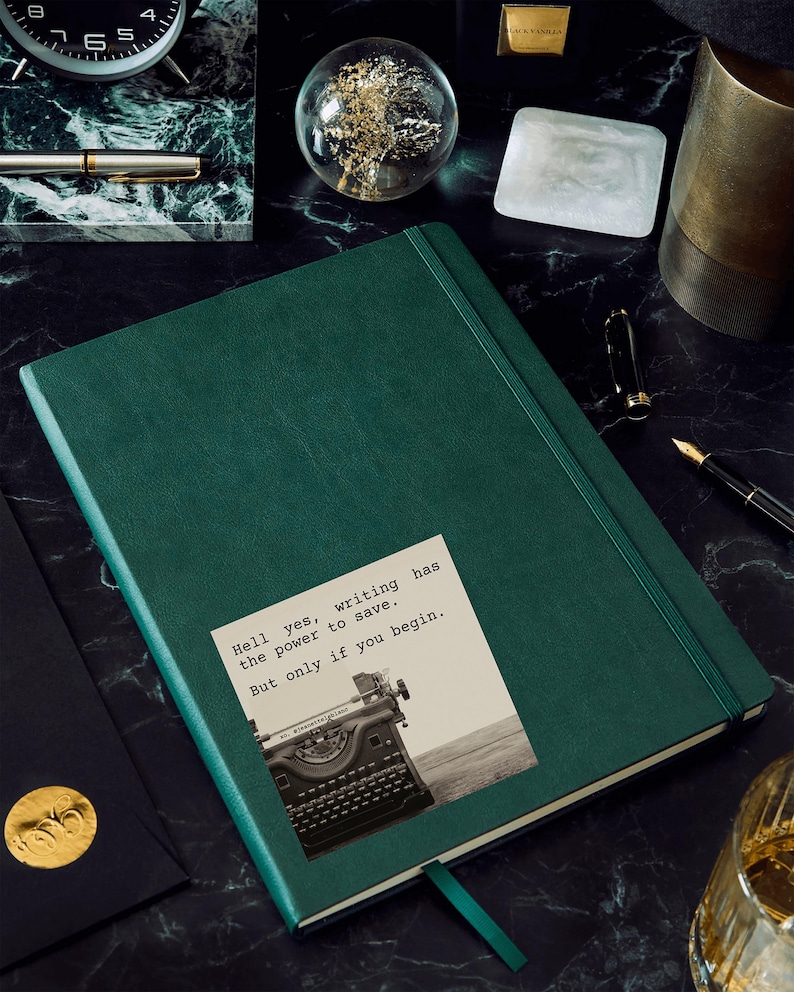 Dark green journal with a sticker reading “Hell yes, writing has the power to save. But only if you begin.” Featuring a vintage typewriter and a Jeanette LeBlanc quote, perfect for writing inspiration and creative motivation.
