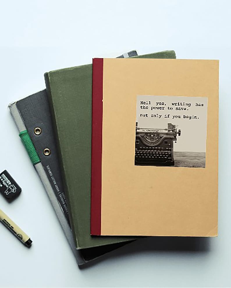A beige notebook with a sepia-toned typewriter sticker sits atop green and gray books. The sticker reads, “Hell yes, writing has the power to save. But only if you begin.”  Jeanette LeBlanc quote writing inspiration & encouragement for storytellers.