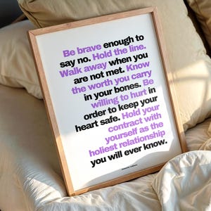 Purple and black boundary print in a light wood frame resting at an angle on rumpled cream bedding against soft beige pillows, in warm morning light. The full text by Jeanette LeBlanc is easy to read, ending with Hold your contract with yourself as the holiest relationship you will ever know. A bedroom wall art reminder for someone going through a divorce, to read first thing each day.