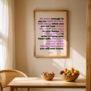 Purple and black boundary print in a light wood frame hanging on a warm beige wall above a light wood dining table with two woven baskets of apples and fruit, a rattan chair, and a sunlit sheer curtain. The purple line Walk away when you are not met reads clearly from across the room. A dining room or kitchen spot for a printable quote that the whole household sees each day.
