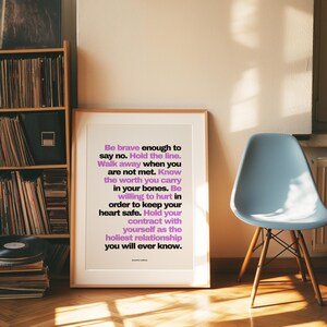 Purple and black boundary print in a light wood frame with a wide white mat leaning on a herringbone floor beside a pale blue molded chair with wood legs and a tall shelf of vinyl records. Warm late sun and window shadows stretch across the floor. A mid century look for a music lover, and a resilience print for a friend who is learning to walk away when she is not met.