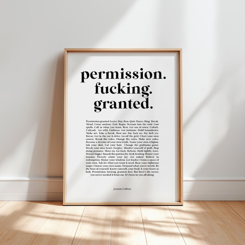 Framed typographic art print featuring the quote: ‘permission. fucking. granted.’ in bold black serif type on a warm white background, by Jeanette LeBlanc. Beneath the headline, a dense permission-list manifesto expands on boundaries, self-trust, creativity, healing. Shown in a light wood frame leaning against a white wall above a sunlit wood floor with soft window shadows. A bold piece for therapy offices, desks, studios during burnout, breakup, reinvention.