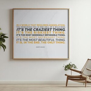 You Remaining You printable shown in a thin light wood frame hanging on a white wall in a bright, airy room, above a pale floor and beside a wood and woven lounge chair with a small plant, with a leafy branch on the left and a tall window on the right. Minimalist decor for a calm living room. A gallery wall print with inner strength in every line, from you remaining you is one hell of a wild ride to the final words.