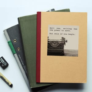 Pu&ograve; includere: Una pila di quaderni con una citazione sulla scrittura sul quaderno in cima. La citazione dice "Hell yes, writing has the power to save. But only if you begin."