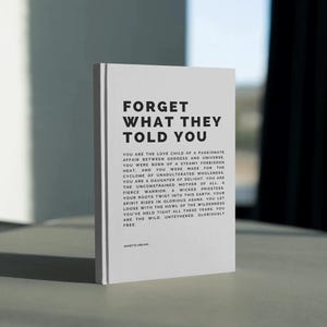 May include: A white book with the title "FORGET WHAT THEY TOLD YOU" in bold black letters. The book's pages contain inspirational text. The book is standing upright on a light-colored surface.
