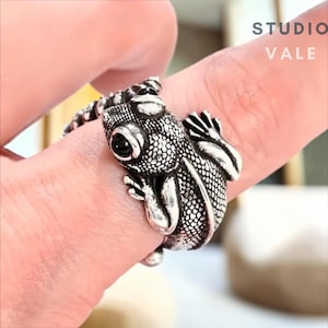 Op de afbeelding: Een zilverkleurige ring in de vorm van een hagedis die om een vinger krult, met getextureerde schubben en donkere, gepolijste ogen. De tekst STUDIO VALE is zichtbaar in de rechterbovenhoek. Het ontwerp toont de kop, poten en staart.