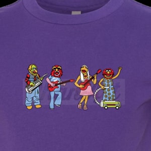 Pode incluir: Camiseta roxa com um gráfico de quatro personagens dos Muppets tocando instrumentos. Os personagens são Animal, Dr. Bunsen Honeydew, Beaker e Miss Piggy.
