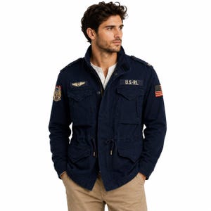 May include: A navy blue field jacket featuring a stand-up collar, four front flap pockets, and a drawstring waist. The jacket displays a U.S.-RL patch, a winged emblem, a colorful crest on the right sleeve, and a small American flag on the left sleeve.