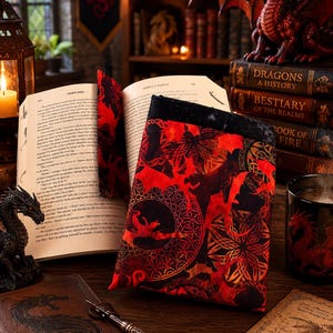 May include: A fabric book sleeve featuring a vibrant red and black dragon pattern with intricate circular geometric motifs. The sleeve is rectangular with a black top edge, designed to protect a book, and is displayed alongside a matching bookmark.