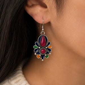 May include: A silver-toned dangle earring featuring a central teardrop-shaped magenta stone surrounded by smaller, colorful enamel accents in navy blue, green, and orange, all set within a decorative metal frame with a hook-style closure.