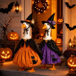 May include: Two white geese dressed in Halloween costumes. One goose wears an orange dress with a black cat print and a black hat with flowers. The other goose wears a purple dress with a black cat print and a black hat with a purple flower.
