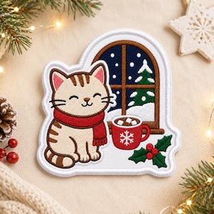 May include: A decorative embroidered patch featuring a light brown tabby cat with dark brown stripes wearing a red scarf. Next to the cat is a red mug with a white snowflake design and marshmallows, set against a snowy window and holly leaves.