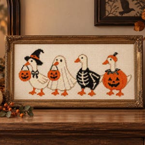 May include: A rectangular cross-stitch embroidery in a gold frame featuring four white geese dressed in Halloween costumes. The geese are wearing a witch hat, a ghost sheet, a skeleton suit, and a pumpkin outfit, each carrying a small orange jack-o'-lantern.