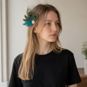 May include: A hair accessory featuring iridescent peacock feathers, teal-colored plumes, and a small cluster of white faux pearls. The decorative piece is attached to a clip, showcasing natural green and blue tones with a central eye pattern.