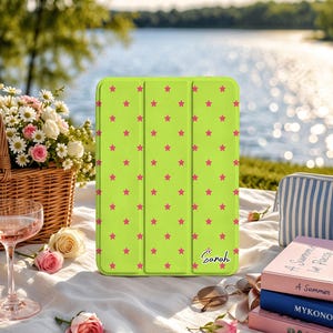 May include: A lime green tablet case featuring a repeating pattern of small pink stars and the name Sarah printed in a black script font. The case has a tri-fold design with vertical creases and a smooth, matte finish on the front surface.