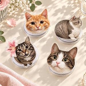 Op de afbeelding: Vier ronde acryl onderzetters met hoge resolutie fotografische prints van katten. Eén toont een oranje cyperse kat, één een zittende grijze cyperse kat, één een bruine cyperse kat met een roze lelie en één een bruin-witte kattenkop.