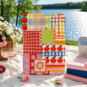 Peut inclure: Une coque de tablette rectangulaire présentant un motif patchwork vibrant avec divers designs incluant des pommes rouges, des carrés à carreaux colorés, un carré vert à damier avec une bordure étoilée, des lapins blancs et un motif floral orange.