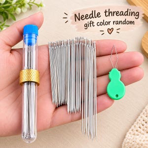 May include: A set of silver sewing needles stored in a clear plastic tube with a blue cap and a gold-colored metal thimble, accompanied by a green gourd-shaped needle threader. The text Needle threading gift color random is visible.