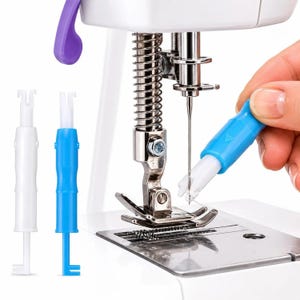 May include: A white and blue plastic needle threader tool shown next to a sewing machine presser foot and needle assembly. The tool features a small hook at one end and a handle, designed to assist in threading a sewing machine needle.