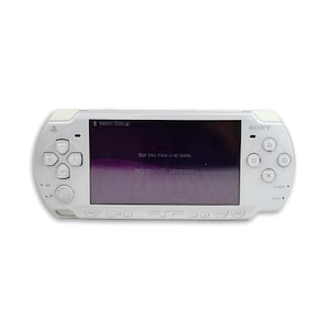 Pode incluir: Uma consola de jogos portátil branca com um ecrã central que apresenta o texto Initial Setup, Set the time and date e 2011/01/01 00:00:00. O dispositivo inclui um pad direcional, quatro botões de ação, um joystick e o logótipo Sony.
