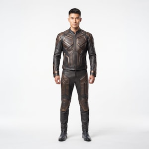 Può includere: Una tuta da moto in pelle nera e bronzo composta da una giacca a maniche lunghe con colletto alla coreana e pantaloni abbinati. La tuta presenta pannelli geometrici strutturati su petto, spalle, braccia e gambe.