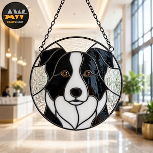Puede incluir: Un atrapasueños circular de vidrieras que presenta el retrato de un perro blanco y negro con ojos de color ámbar. La pieza está construida con bordes de vidrio transparente texturizado y sostenida por una cadena de metal negro. El logo AWL CRAFTS MART es visible.