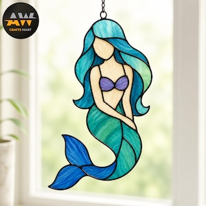 May include: A stained glass suncatcher shaped like a mermaid with flowing teal and blue hair, a purple seashell top, and a green and blue tail. The figure is outlined in black metal and hangs from a small chain, featuring a light cream skin tone.