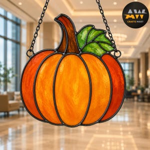 May include: A stained glass pumpkin suncatcher featuring vibrant orange and yellow glass segments with a brown stem and a bright green leaf. The piece is framed in black metal solder lines and hangs from a black metal chain for display.